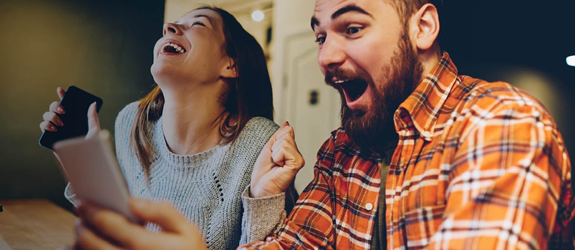A man and a woman checking their mobiles and looking happy.