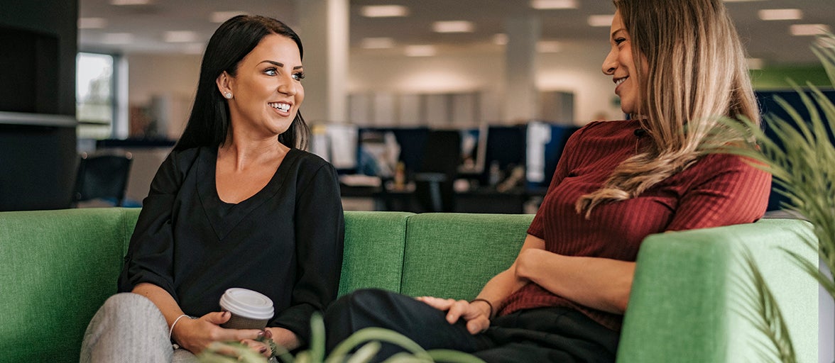 Two colleagues sat on a sofa enjoying a coffee and a chat.