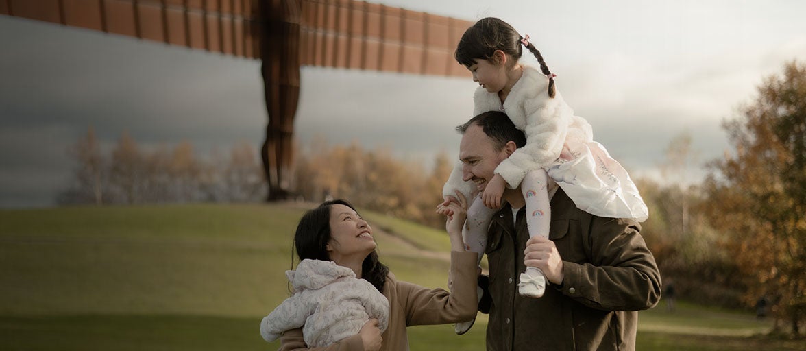 A young family of four walking down a field laughing and smiling with one another. 