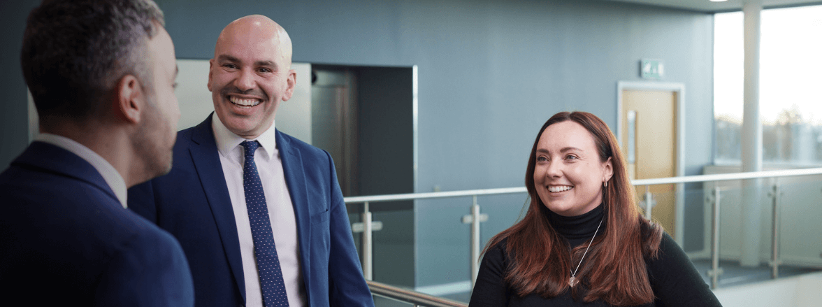 Three professionals smiling inside Newcastle Building Society head office.