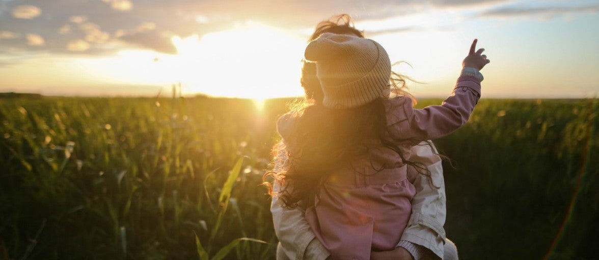 A mother and daughter stand in a field pointing at the sky