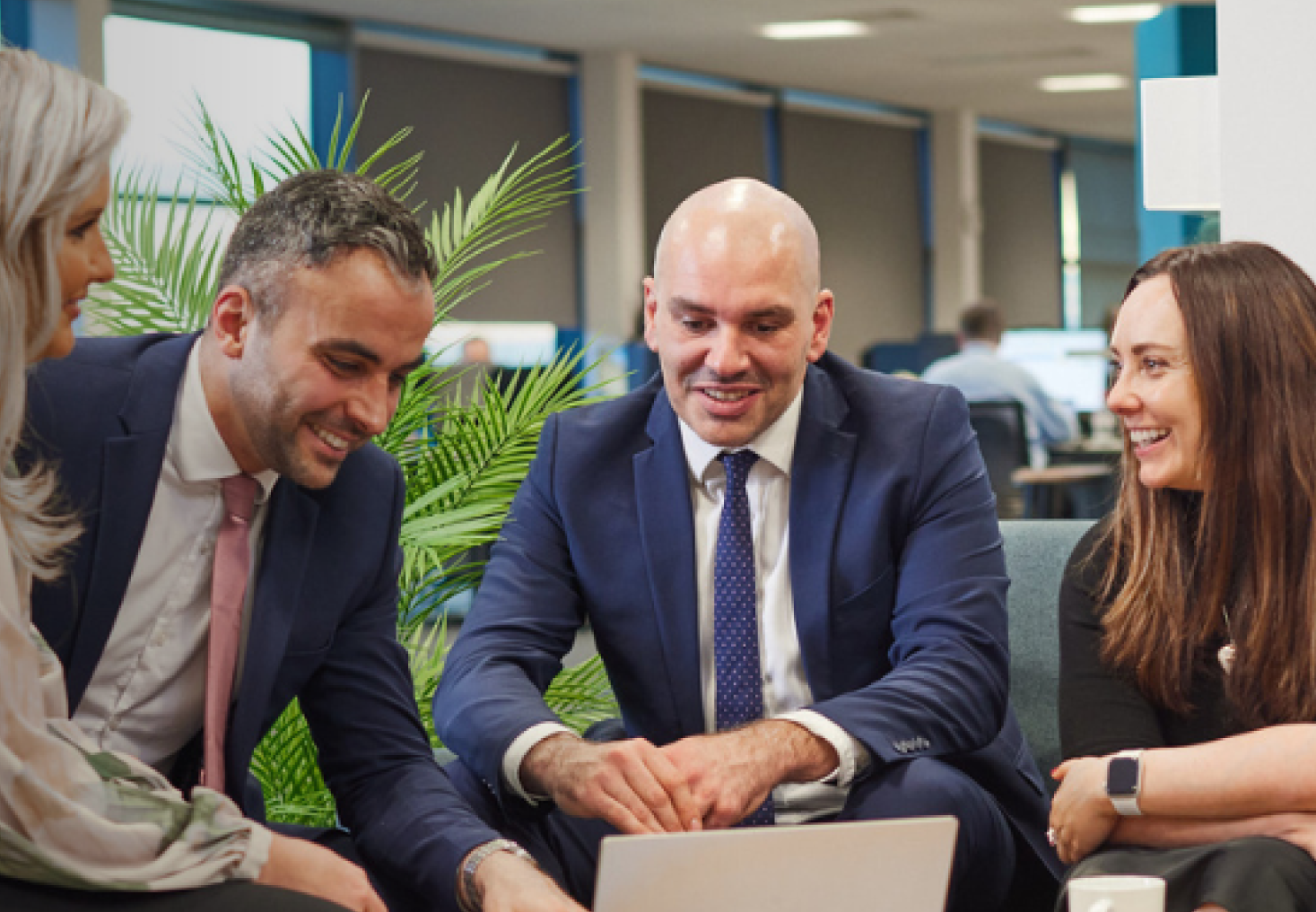 A group of people sitting in a room around a laptop 