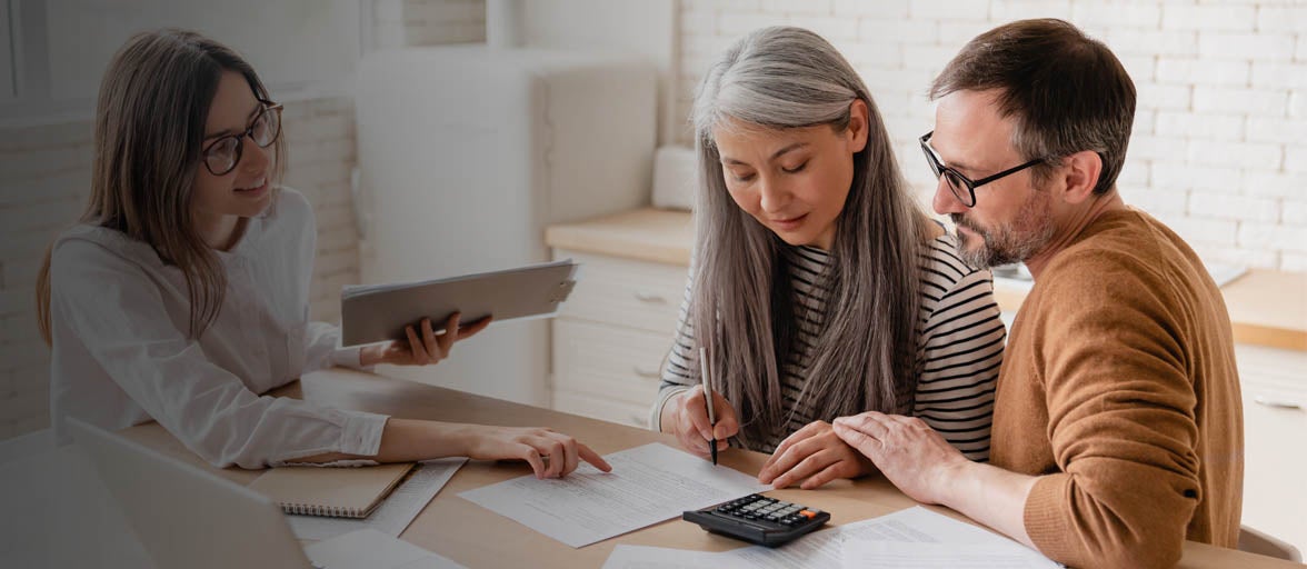 A couple sat at a table looking at documents, accompanied by a Financial Adviser. 
