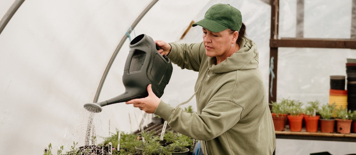 A lady watering some plants using a watering can.