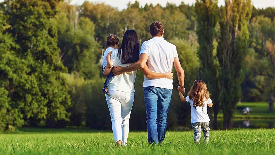 A man and woman holding children's hands, walking in a field, with their backs towards the camera. 