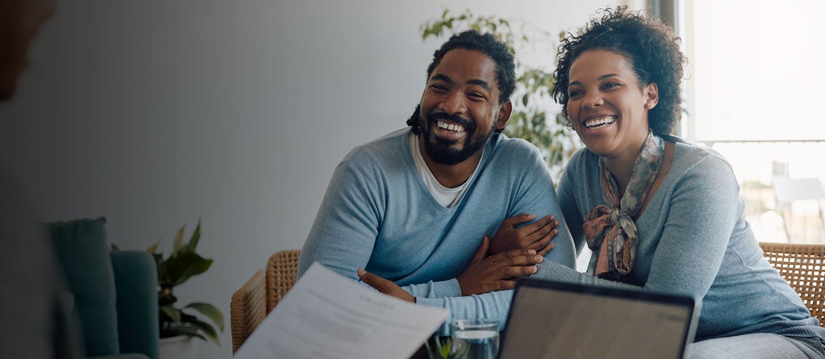A man and woman linking arms sat down happily looking at their financial adviser. 
