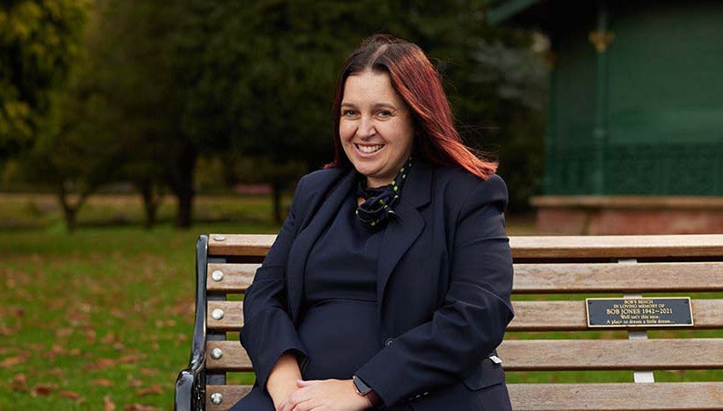 Branch Manager sitting on park bench with trees in background.