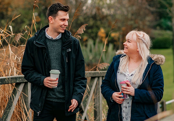 A couple laugh as they walk outside with coffees