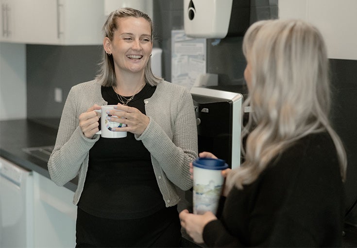 A woman holding a cup of coffee and another woman smiling.
