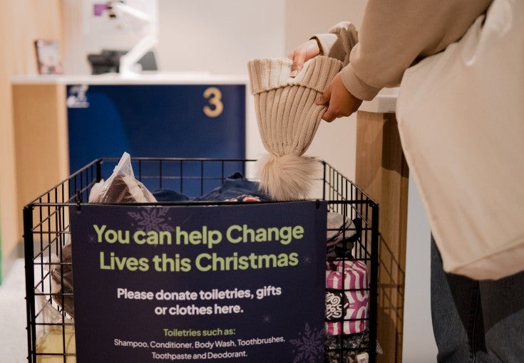 A person dropping a wooly hat into a festive donation bin.