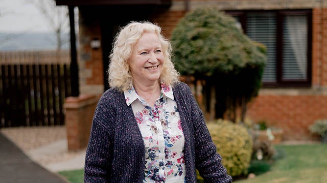 A Newcastle Building Society customer walking in front of her house smiling. 