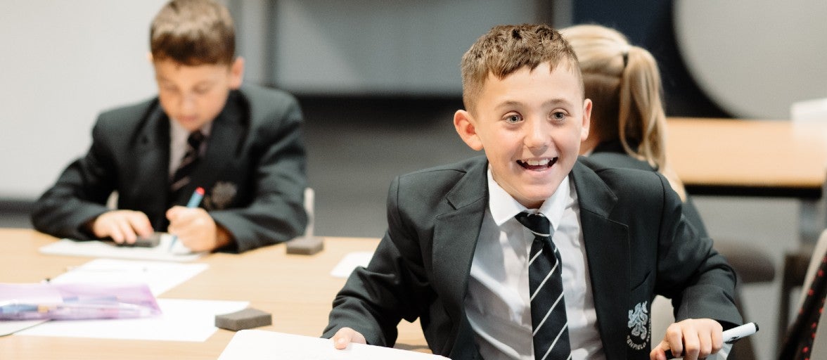 A student in a classroom holding a whiteboard and smiling.