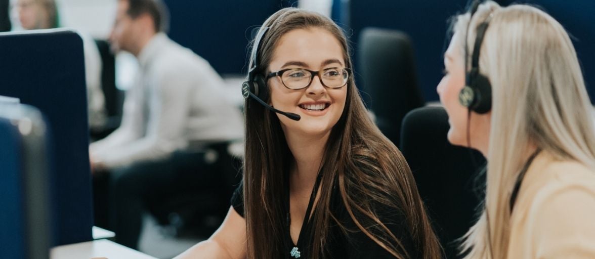 Two women with headsets on chat to each other