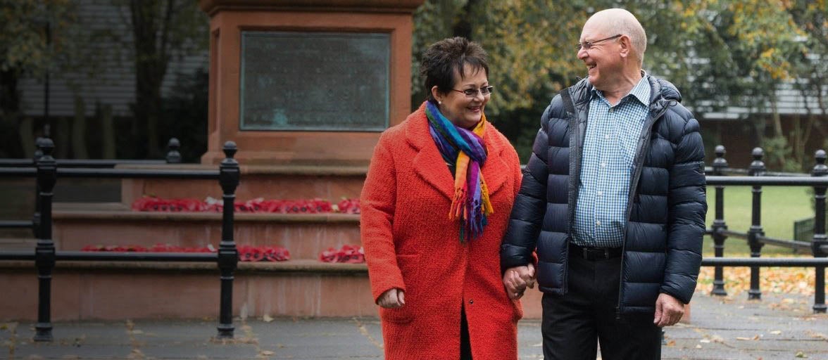 A middle aged couple hold hands by a memorial in Gosforth
