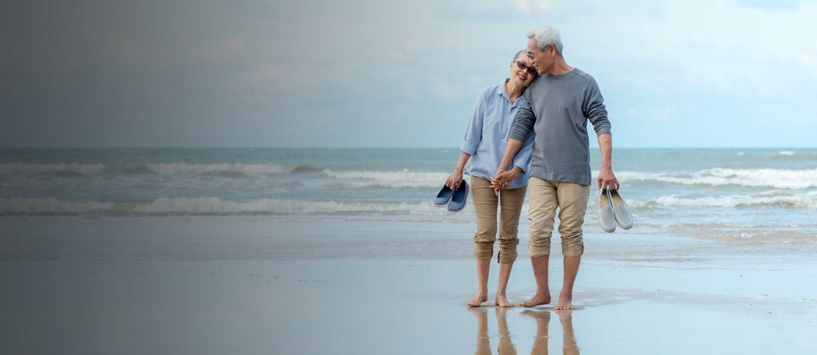 An older couple walking down the beach, holding hands. 