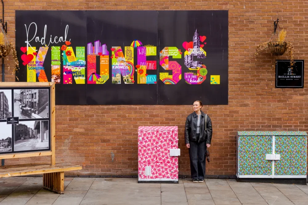 A woman standing in front of a sign that reads radical kindness. 