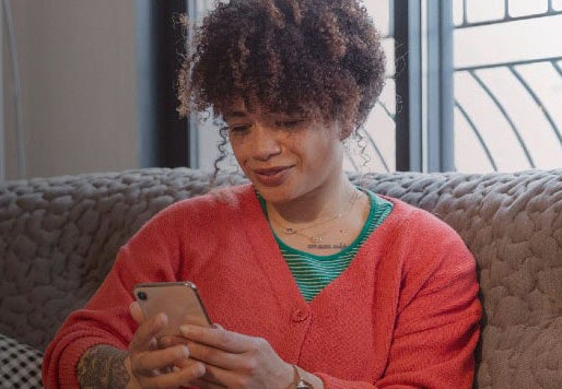 Woman sat on sofa looking at her mobile phone, smiling. 