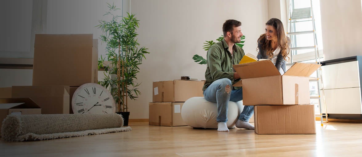A man and woman sitting on a cushion with boxes in the background.