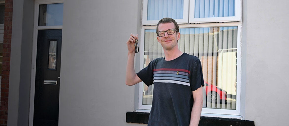 A man holding up a key stood in front of a house 