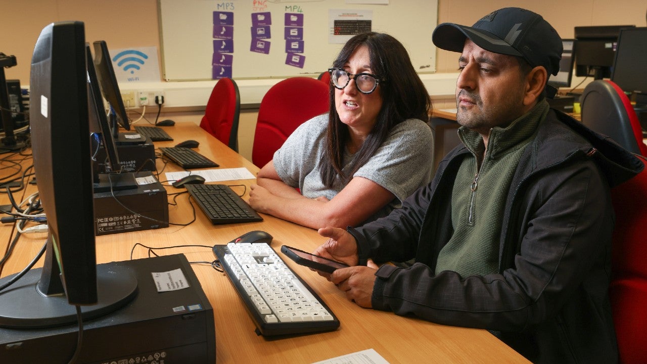 A woman and a man sat at desk together using a computer.