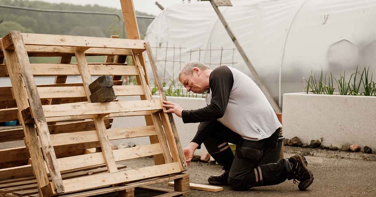 Man kneeling on the floor holding a wooden palette. 