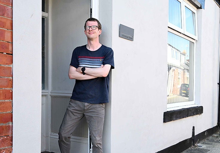 A man stood in the doorway of his house, with his arms crossed. 