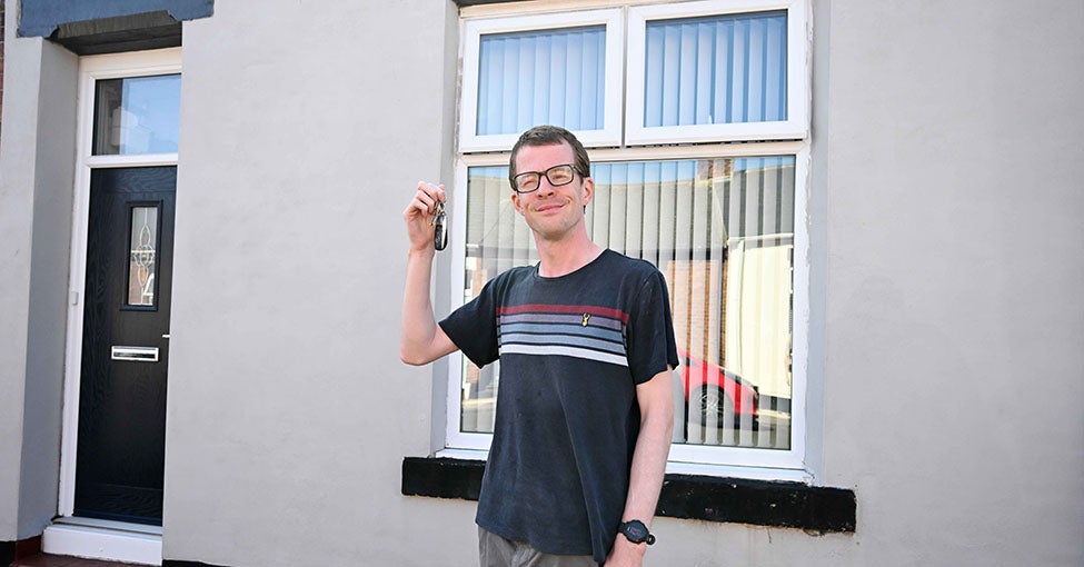 A man holding up a key stood in front of his house.