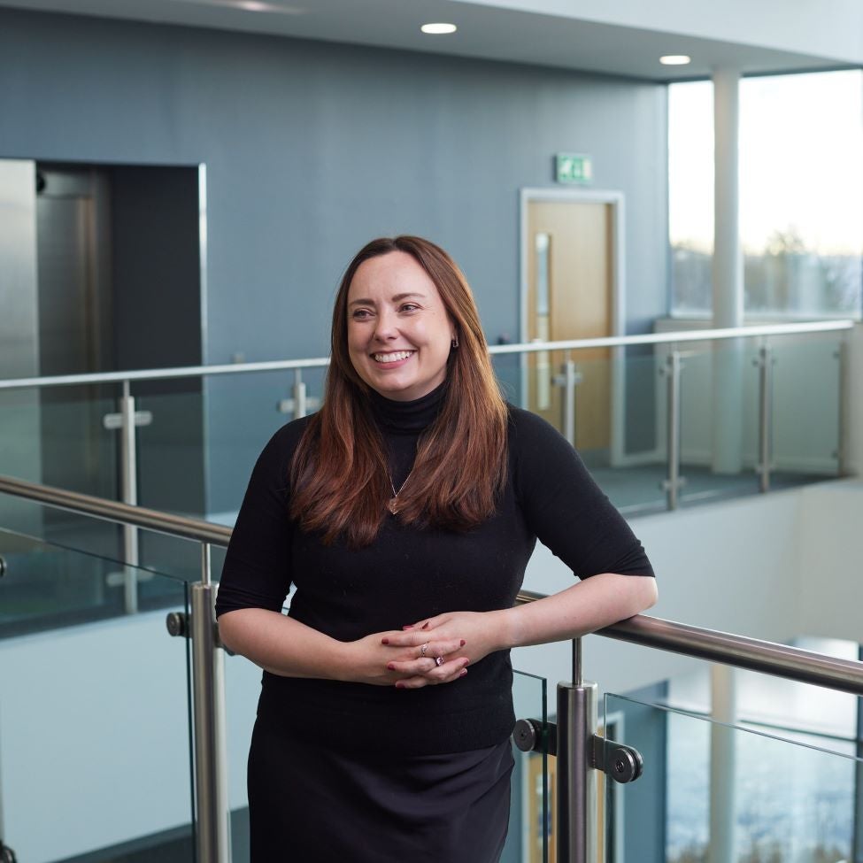 Michelle Ash, National Account Manager, standing in a office hallway in a black dress