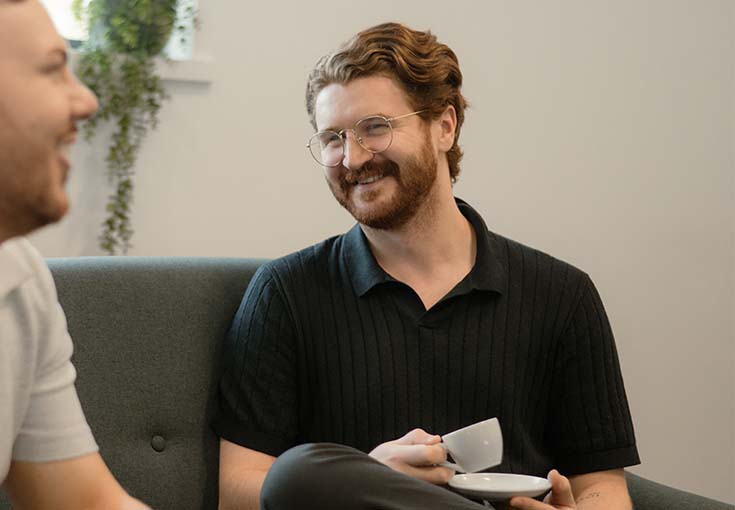 A man sitting on a couch holding a cup and saucer