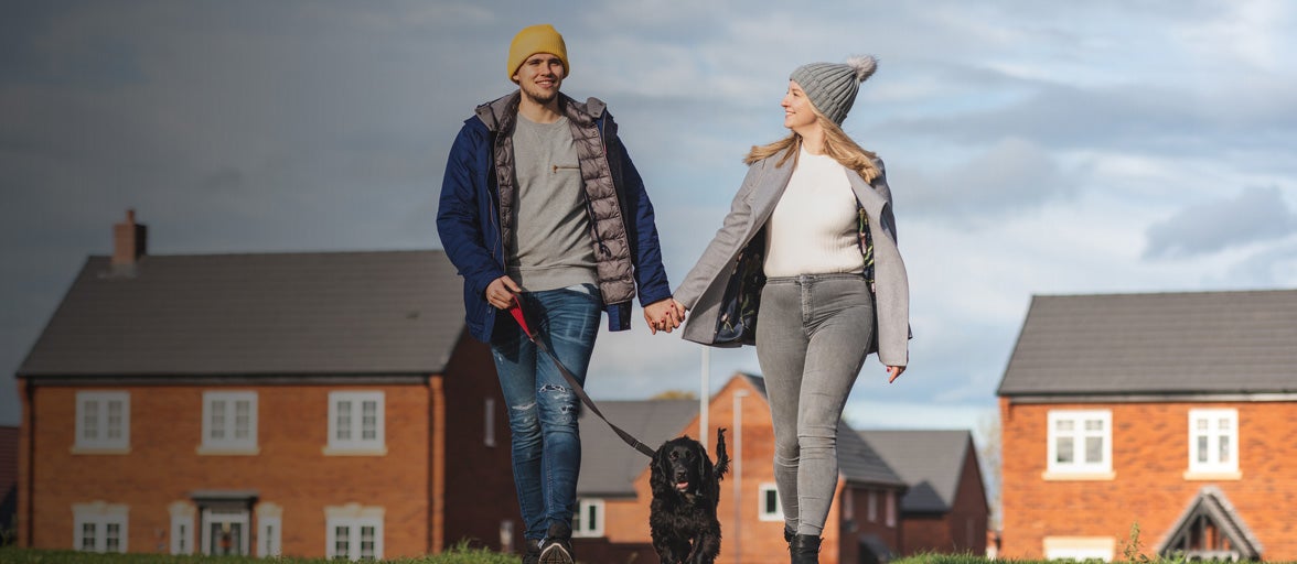 Couple walking their dog in front of some houses. 