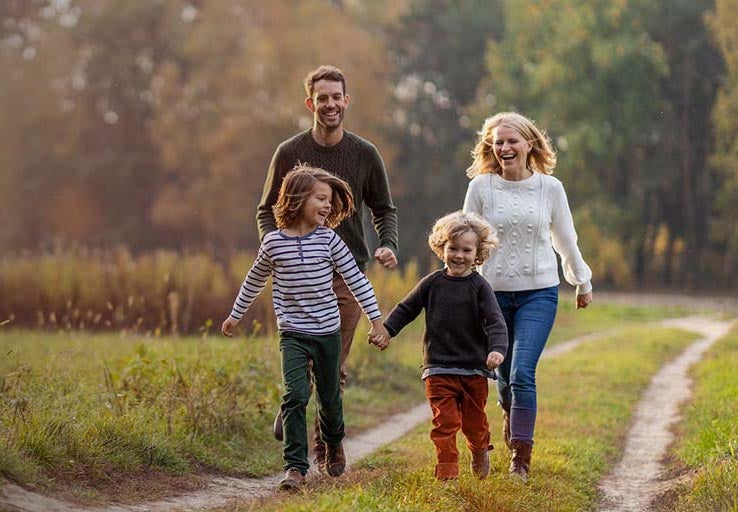 A man and woman running with children along a path, laughing and smiling. 
