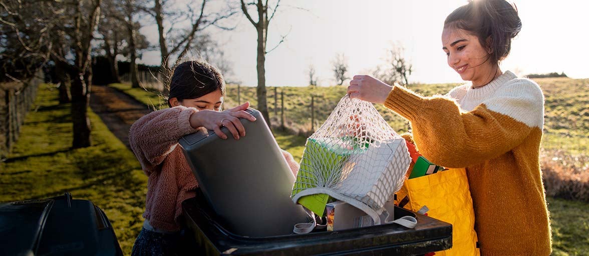 Two girls emptying recycling into a bin outside. 