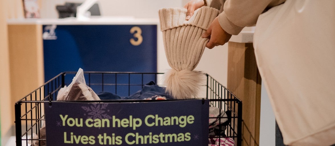 A person dropping a wooly hat into a festive donation bin.