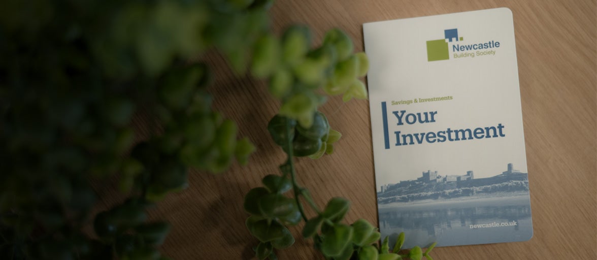 Newcastle Building Society passbook on a table with a green plant to the left of it. 