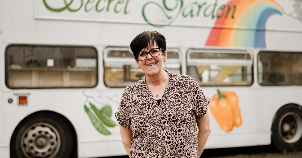 A lady stood with a double decker bus in the background behind her. 
