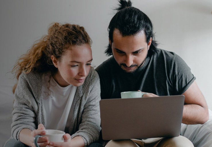 Couple sat on sofa with coffee cups looking at a laptop