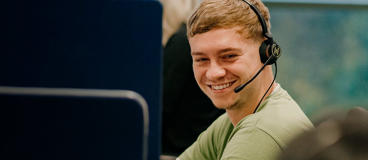 One of the customer service team sat at his desk with a headset on.