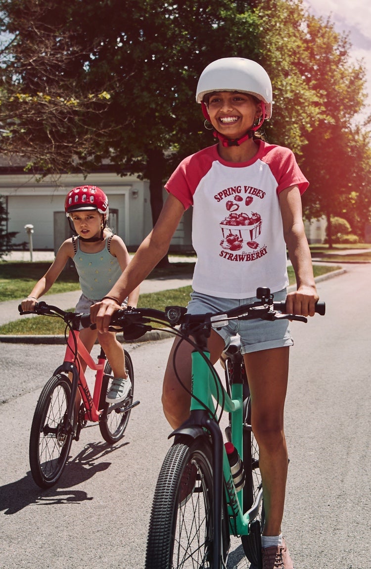 Wide surburban road with four children riding alongside each other on their woom EXPLORE bikes towards the camera.