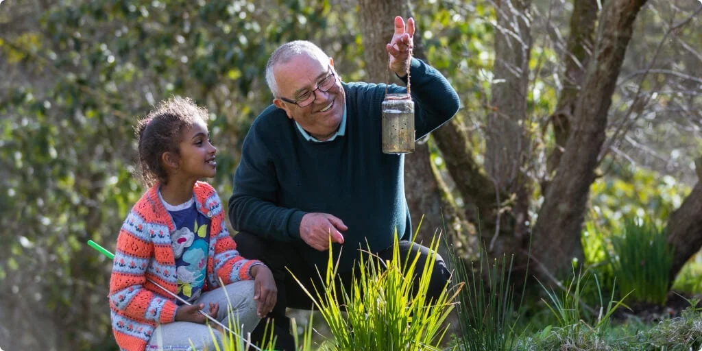 Man collecting insects in a jar showing them off to a young girl. 