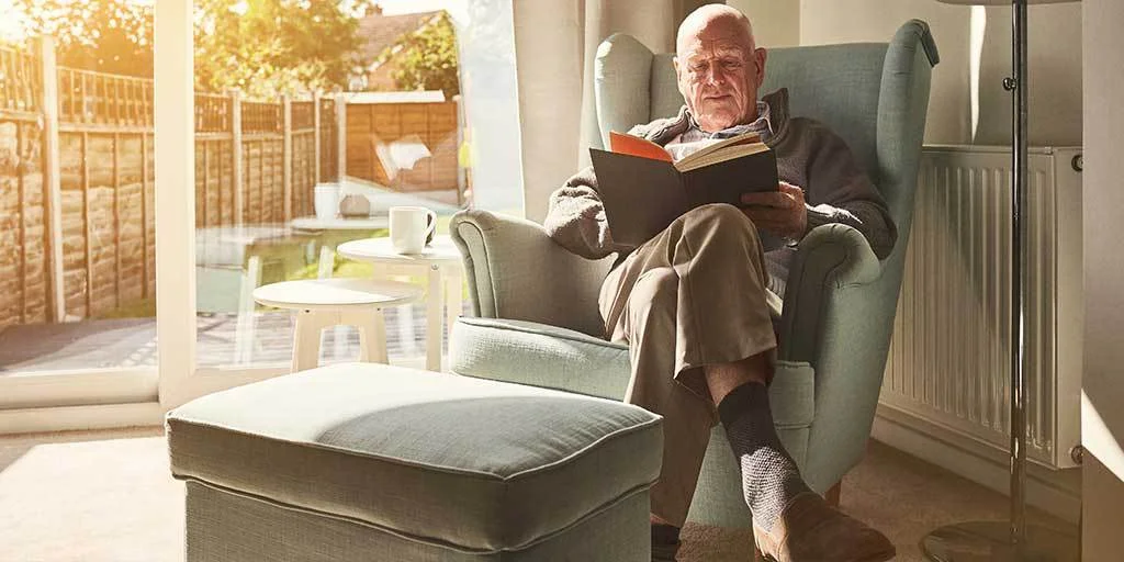 Man comfortably reading book whilst sitting on chair beside patio door