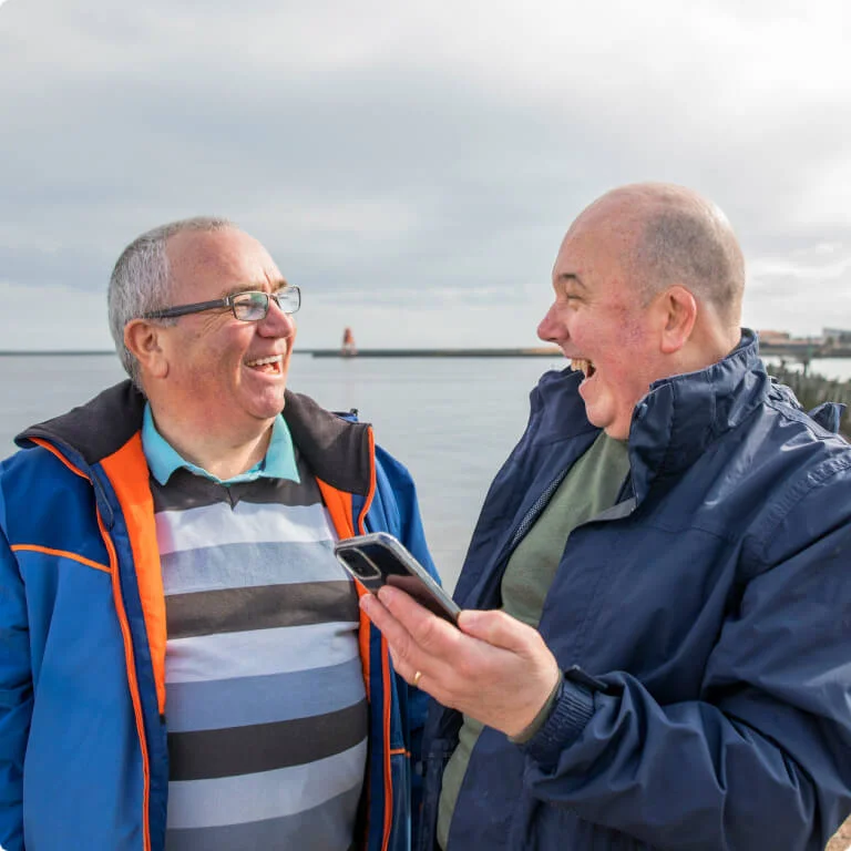 2 friends laughing while one holds his phone out in front.
