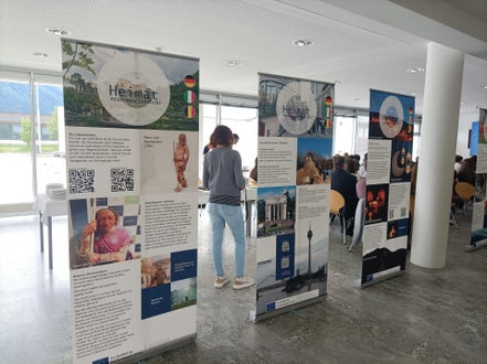 Einblick in die Wanderausstellung „Heimat – regionale Identität in Europa“ mit Publikum im Hintergrund bei der Ausstellungseröffnung am 05.05.2025 im Oberschulzentrum Mals. Foto: FS Tisens.