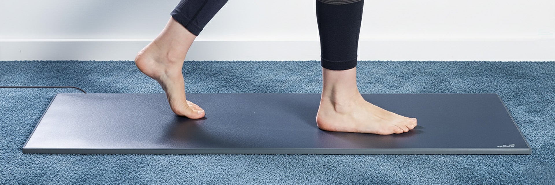 A barefoot woman walking on the Materialise Footscan Pro Level pressure plate in a room with blue carpet.