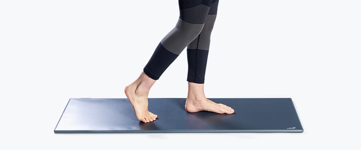 A barefoot woman walking on the Materialise Footscan Pro Level pressure plate against a white backdrop.
