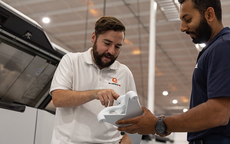 An Endeavor 3D team member holding a white 3D-printed part whild another team member points to a component of the part