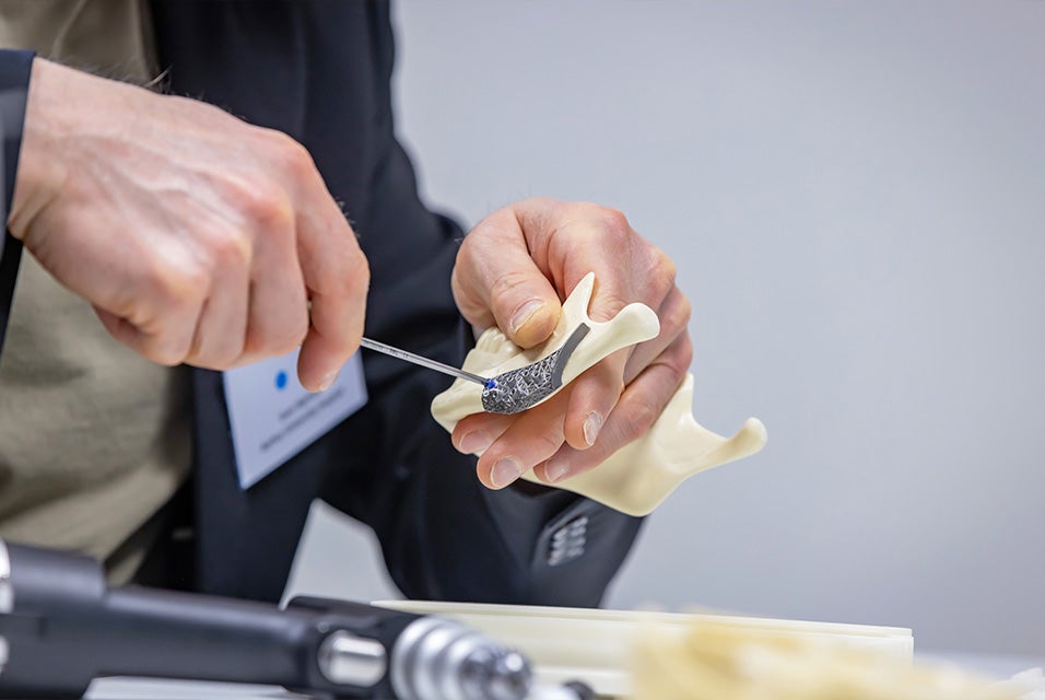 Hands demonstrating the placement of a porous fixation plate on a jaw bone model using a surgical instrument during a Materialise Dry Bone Training.
