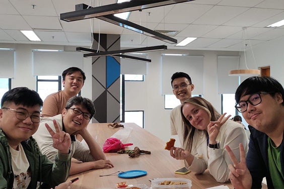 The Mimics Enlight CMF software development team in Malaysia. Five men and one woman are in the canteen area doing peace hand gestures.