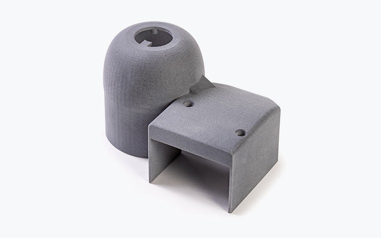 A cylindrical plastic 3D-printed part connected to an open cube-shaped part, printed in PA 12S using Multi Jet Fusion