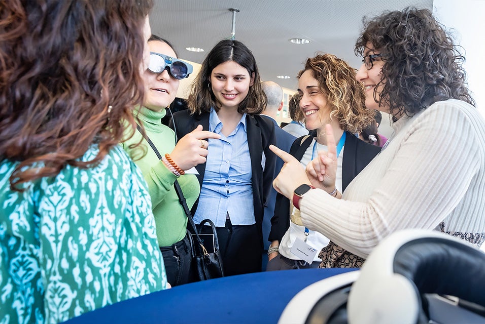 Five women standing in a group, with one woman wearing augmented reality goggles.