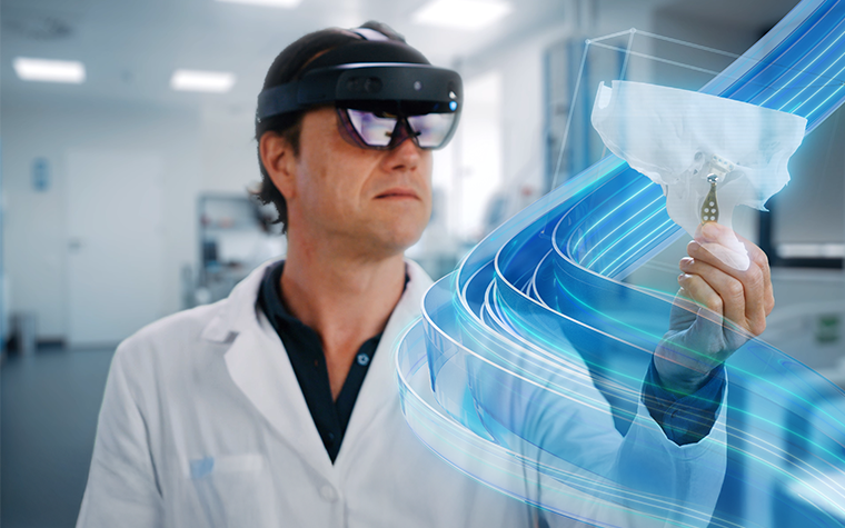 A surgeon wearing Microsoft Hololens augmented reality glasses and interacting with a virtual model of a patient's skull with a 3D-printed TMJ implant. The Mimics branded blue swirl is flowing around the model.